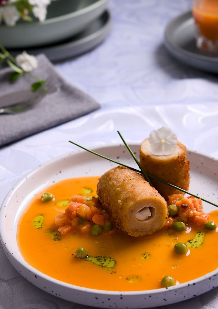 Elegant plated dish with rolled chicken and vibrant soup garnish.